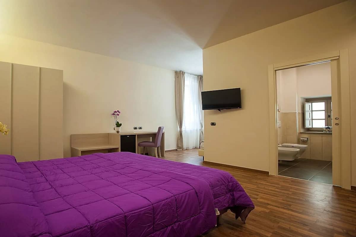 A bedroom with a large bed, a desk, a chair, a television, and a bathroom.