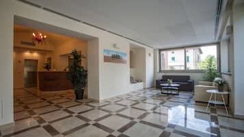Un hall de hotel con suelo a cuadros, una recepción, una araña y una zona de estar con sofá y mesa de centro.