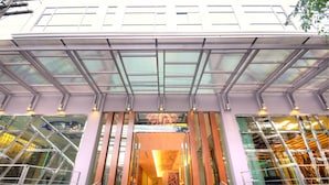 A modern building entrance with a glass facade, a covered walkway, and a staircase leading to the entrance. - One One Bangkok Hotel (Bangkok)