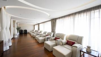 Amplia habitación de hotel moderna con una hilera larga de sofás de cuero, piso de madera y ventanas grandes con cortinas.