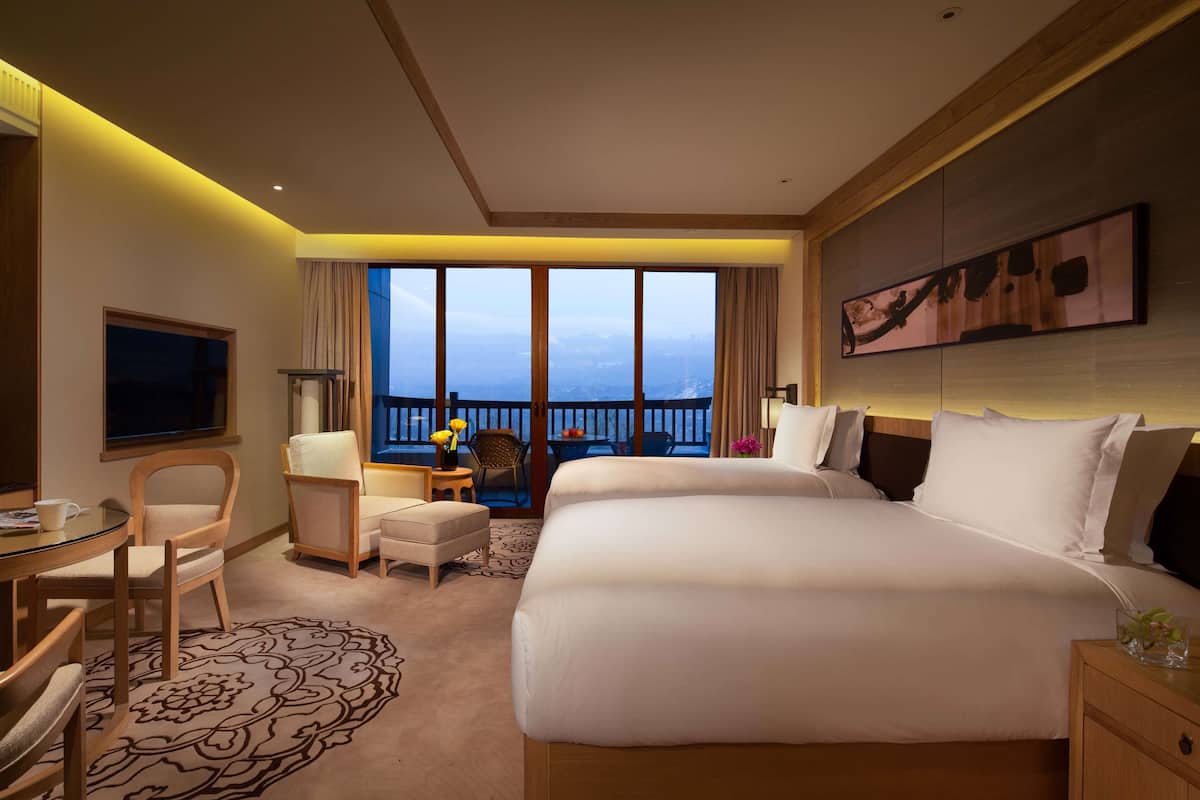 A hotel room with a large bed, a desk, a chair, a television, and a balcony with a view.