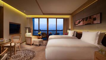 A hotel room with a large bed, a desk, a chair, a television, and a balcony with a view.