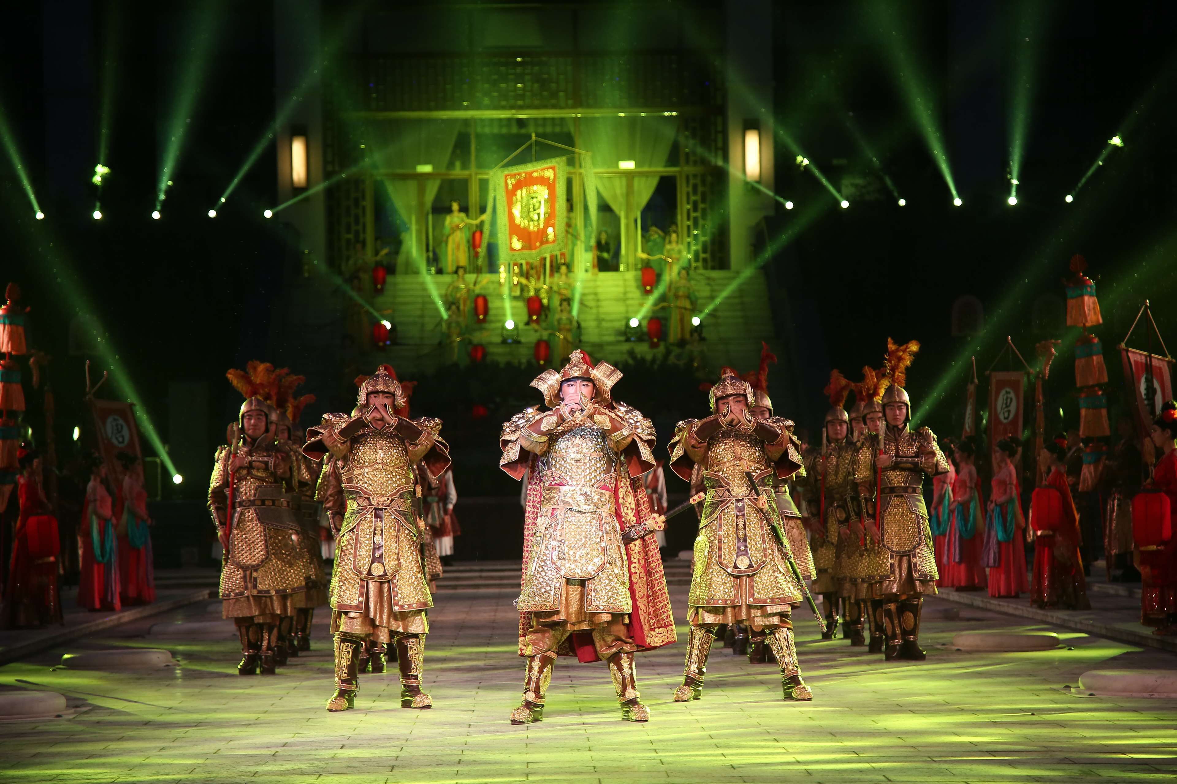 A group of people in elaborate costumes walking on a stage with a backdrop of traditional architecture.