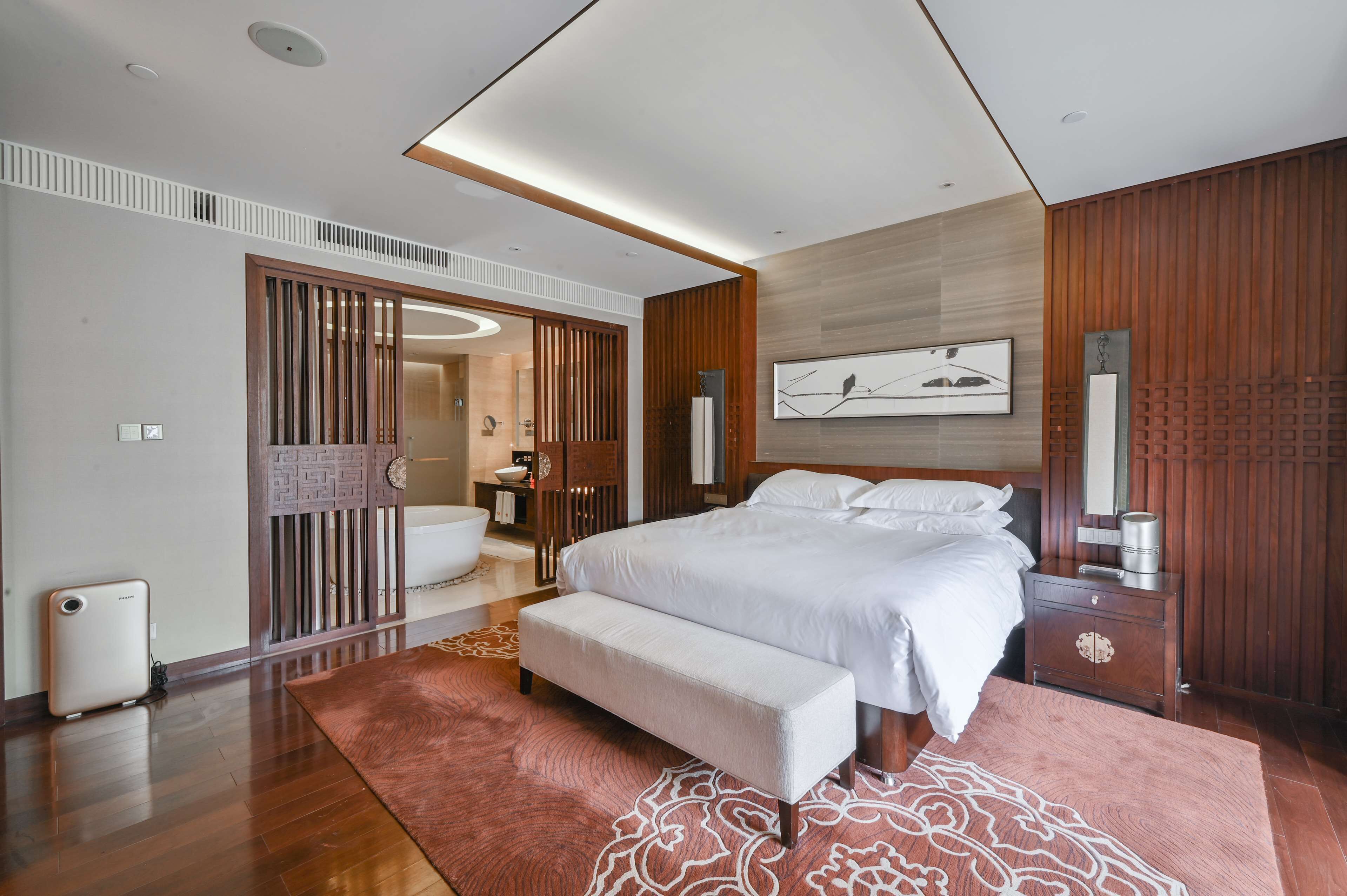 Un dormitorio moderno con una cama grande, un banco, una mesita de noche y una pared de paneles de madera.