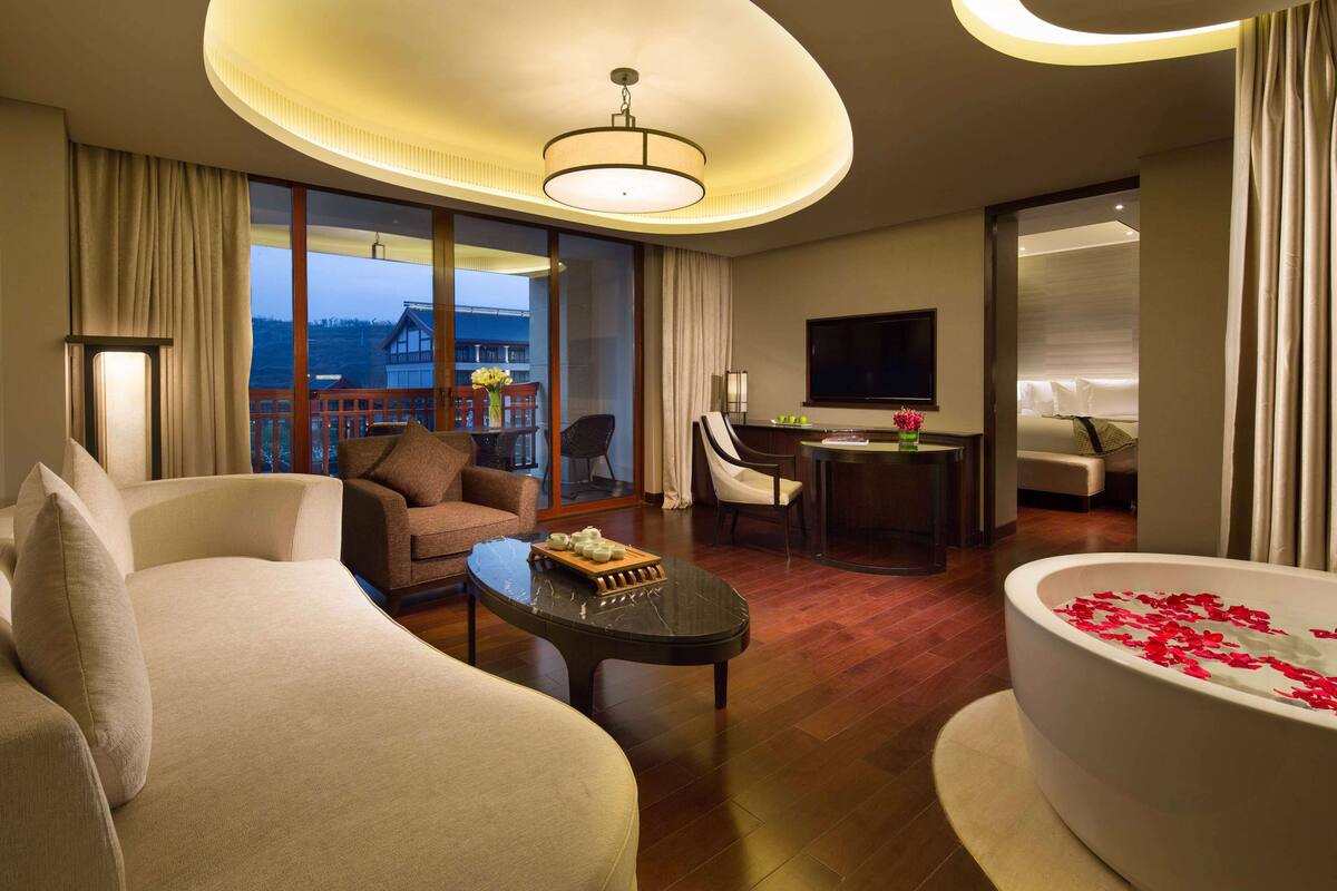 A hotel room with a large bed, a sofa, a coffee table, a TV, and a bathtub with rose petals.