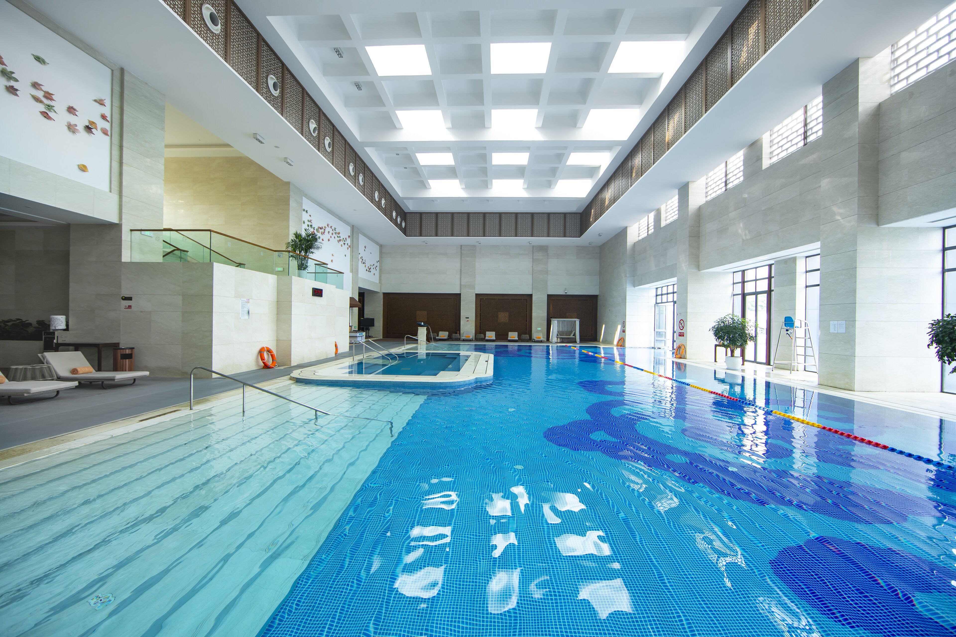 Una amplia piscina interior con agua cristalina, una plataforma de clavados central y un diseño arquitectónico moderno con techo alto y luz natural.