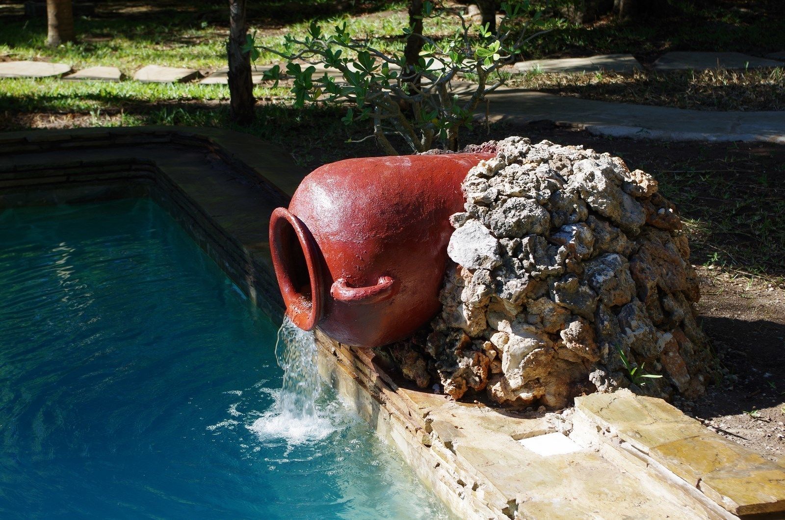 A red ceramic pot over a stone wall next to a swimming pool.