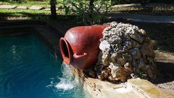 A red ceramic pot over a stone wall next to a swimming pool.