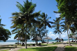 Una playa con palmeras, chozas de techo de paja y una vista despejada del océano.