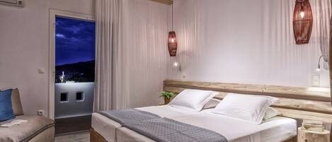 Une chambre à coucher avec un grand lit, deux tables de chevet, une commode, une fenêtre avec des rideaux et une vue sur l’extérieur.