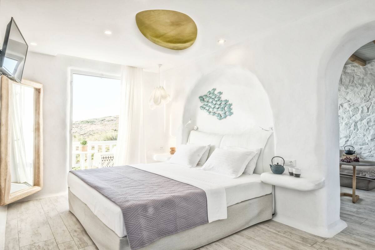 Un dormitorio moderno con una cama grande, una mesita de noche, un televisor montado en la pared y vistas al exterior.