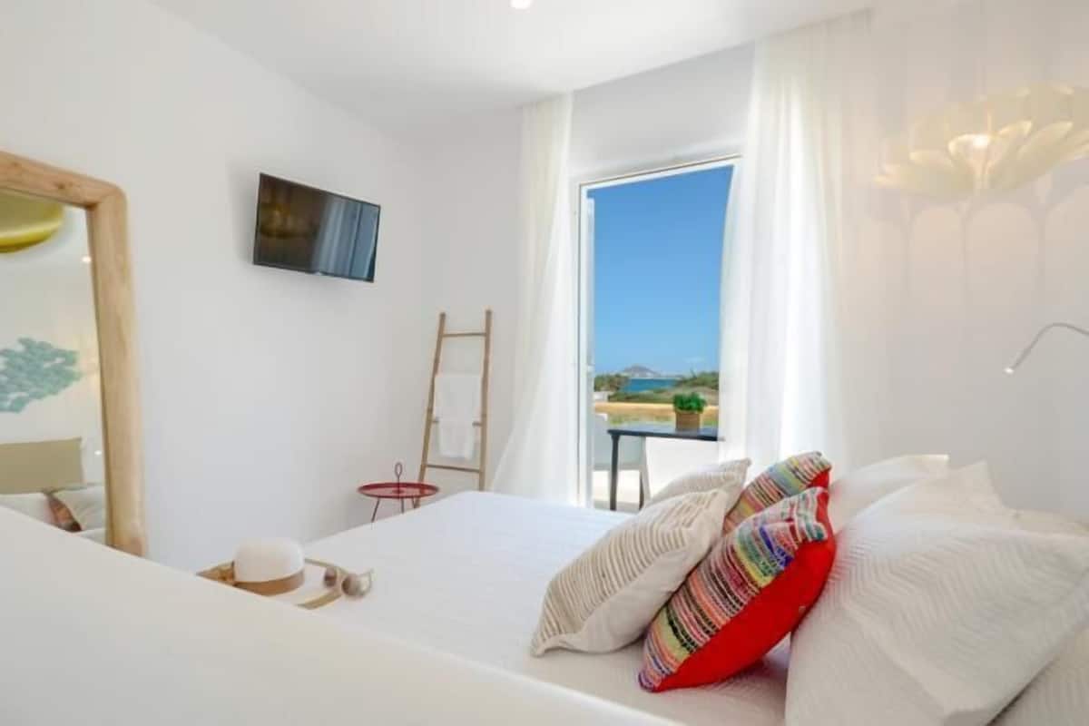 Un dormitorio con cama, espejo, una mesita, una escalera y una ventana con vista al mar.