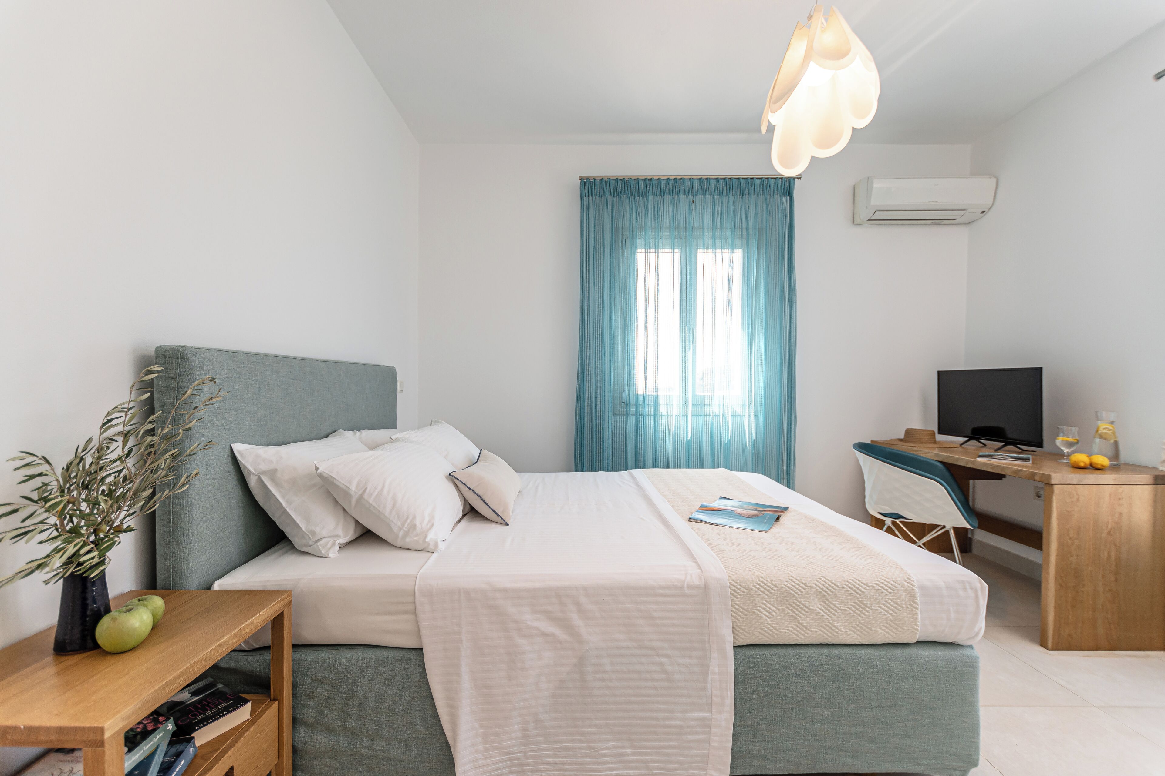 A modern hotel room with a bed, a desk, a chair, a TV, and a window with curtains.