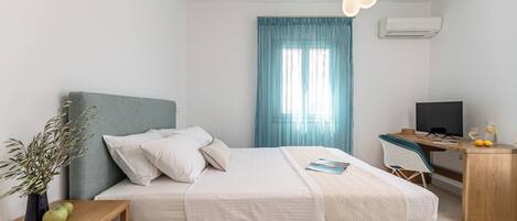 A modern hotel room with a bed, a desk, a chair, a TV, and a window with curtains.