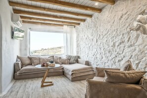 A cozy living room with a stone wall, wooden beams, a large window, and a sectional sofa.