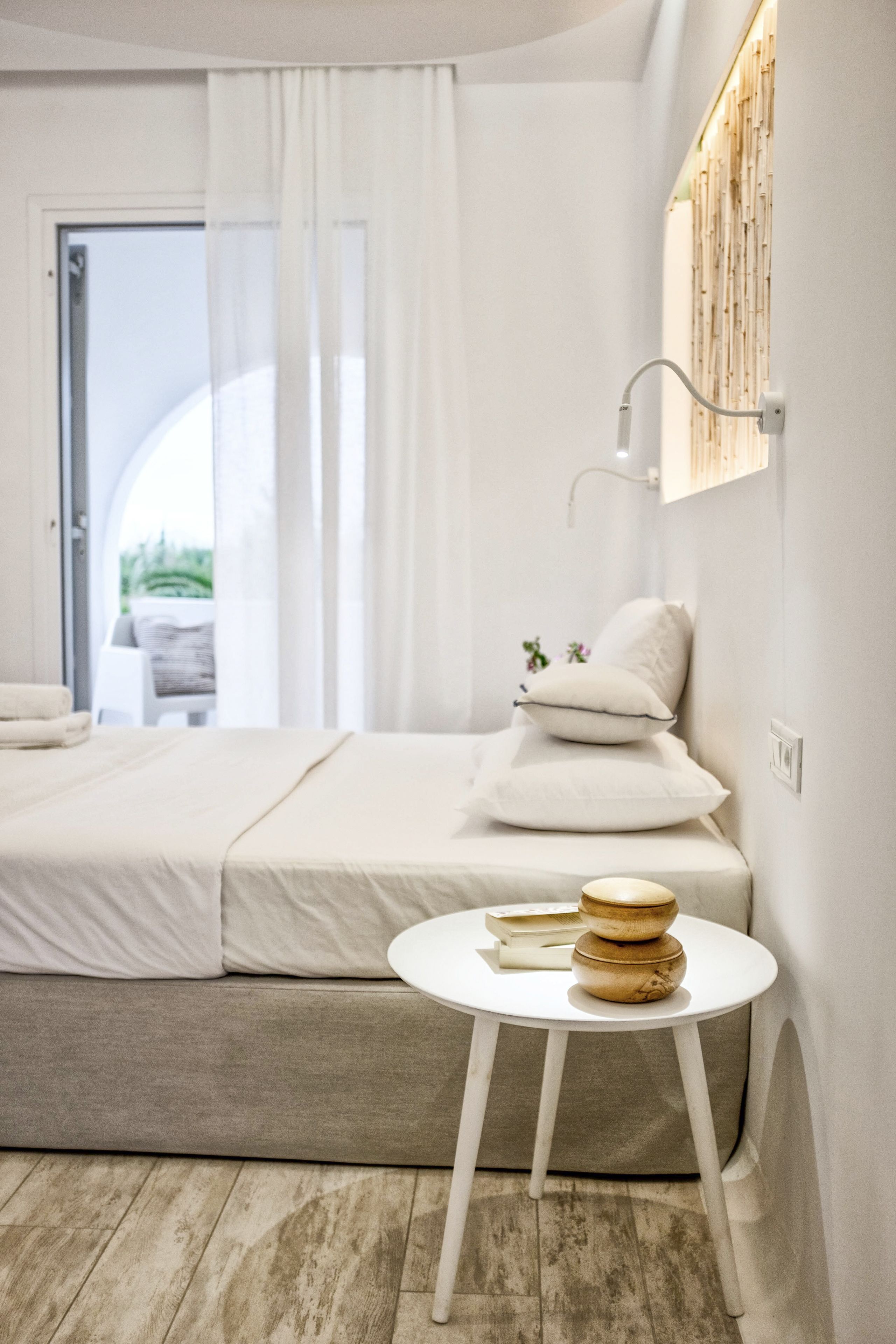 A modern bedroom with a bed, a bedside table with books, and a view of the outdoors.