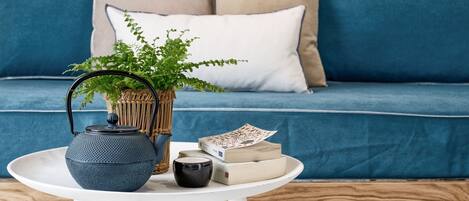 A modern living room with a blue sofa, a round white table, a blue teapot, a wicker plant pot, and a patterned wall.