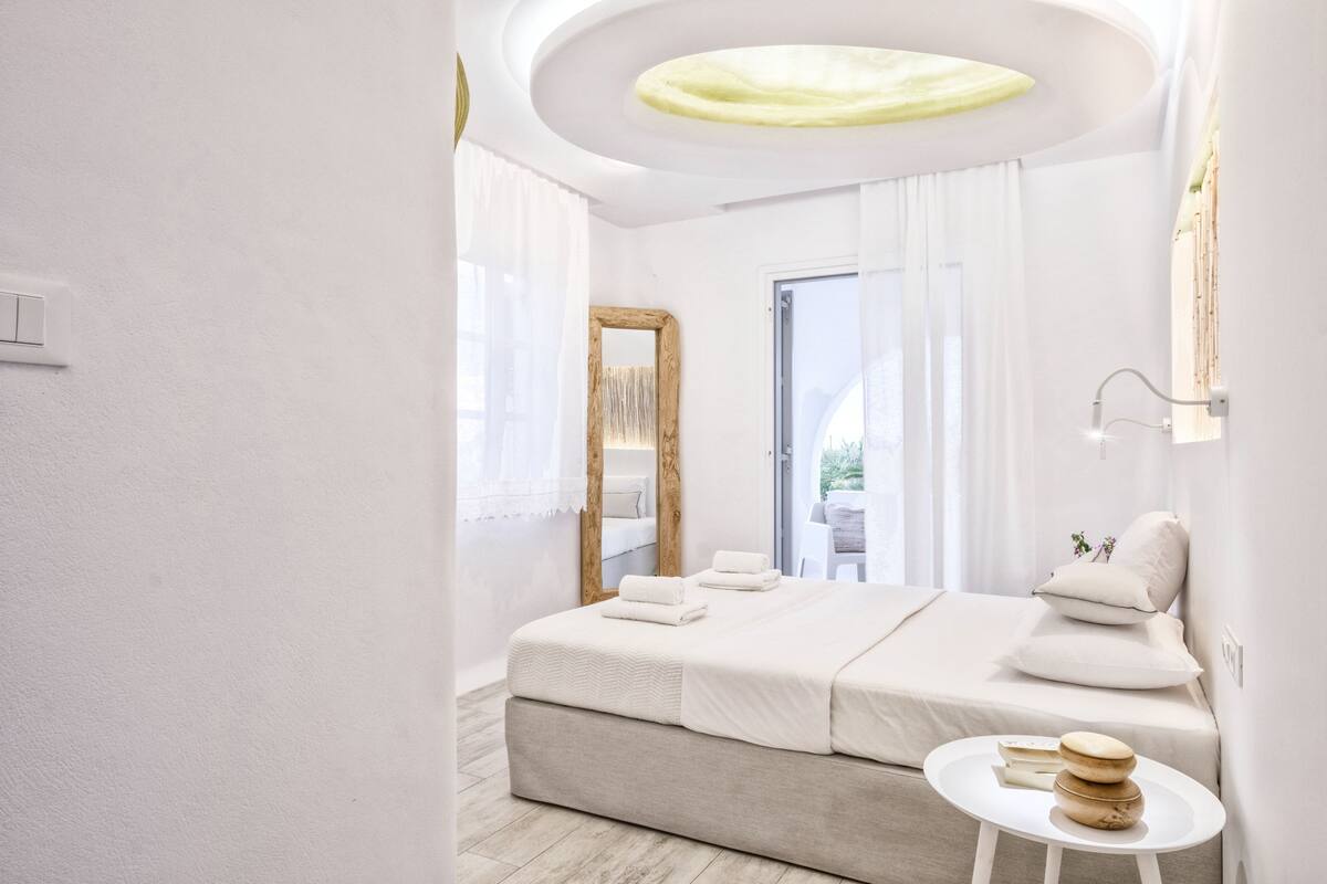 Un dormitorio moderno con una cama grande, una mesa redonda con libros y vistas al exterior.