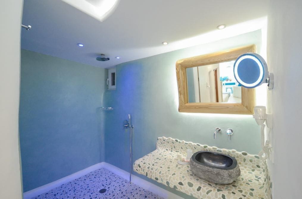 Une salle de bain avec une douche, un lavabo doté d’un receveur en pierre et un miroir avec un cadre en bois.