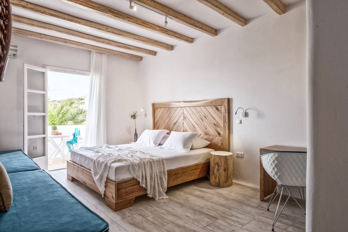 Un dormitorio con cama de madera, una pequeña mesa redonda y vistas al exterior con zonas verdes.