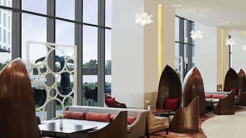 A modern hotel lobby with large windows, a seating area with unique chairs, and a decorative wall.