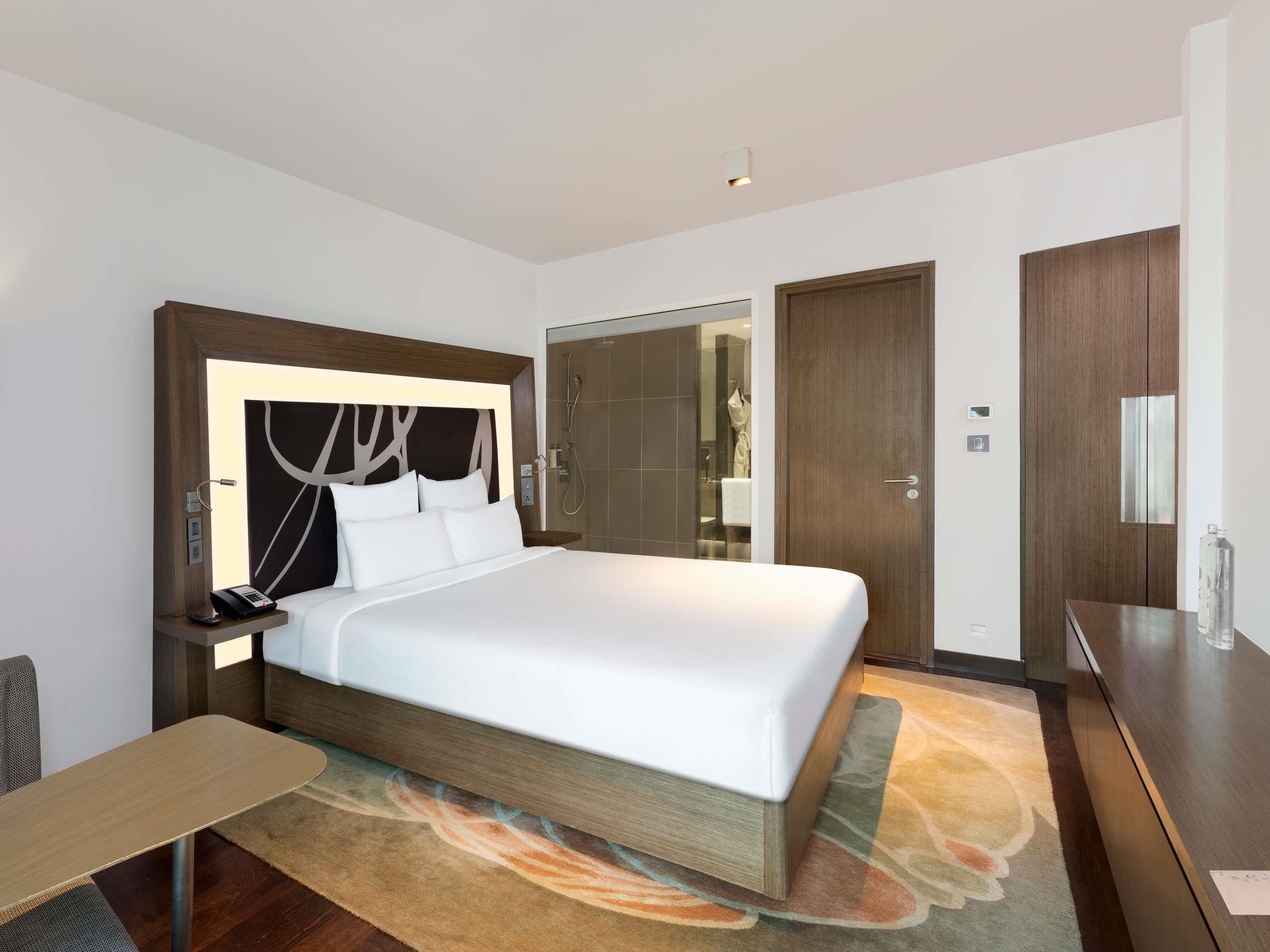 A hotel room with a large bed, bedside table, nightstand, and a mirror.