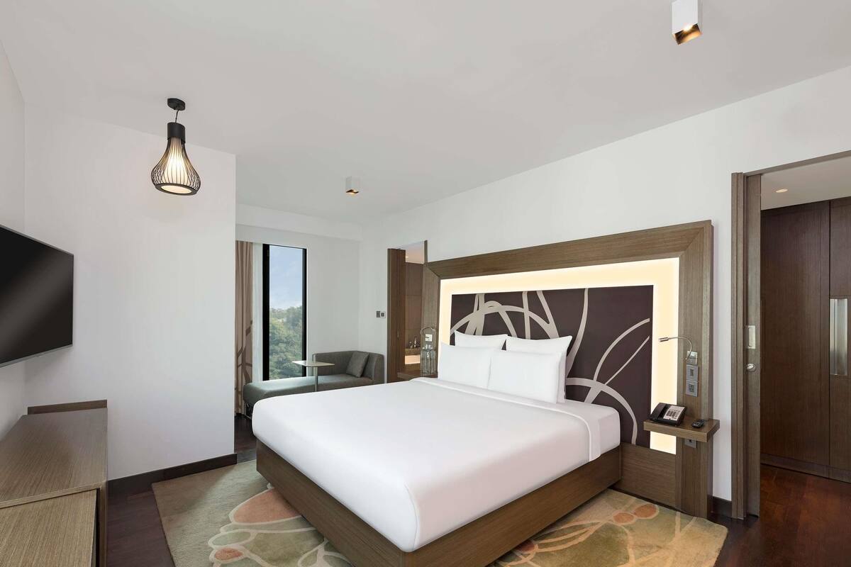 Een moderne hotelkamer met een groot bed, een flatscreen televisie, een bureau en een zithoek met uitzicht.
