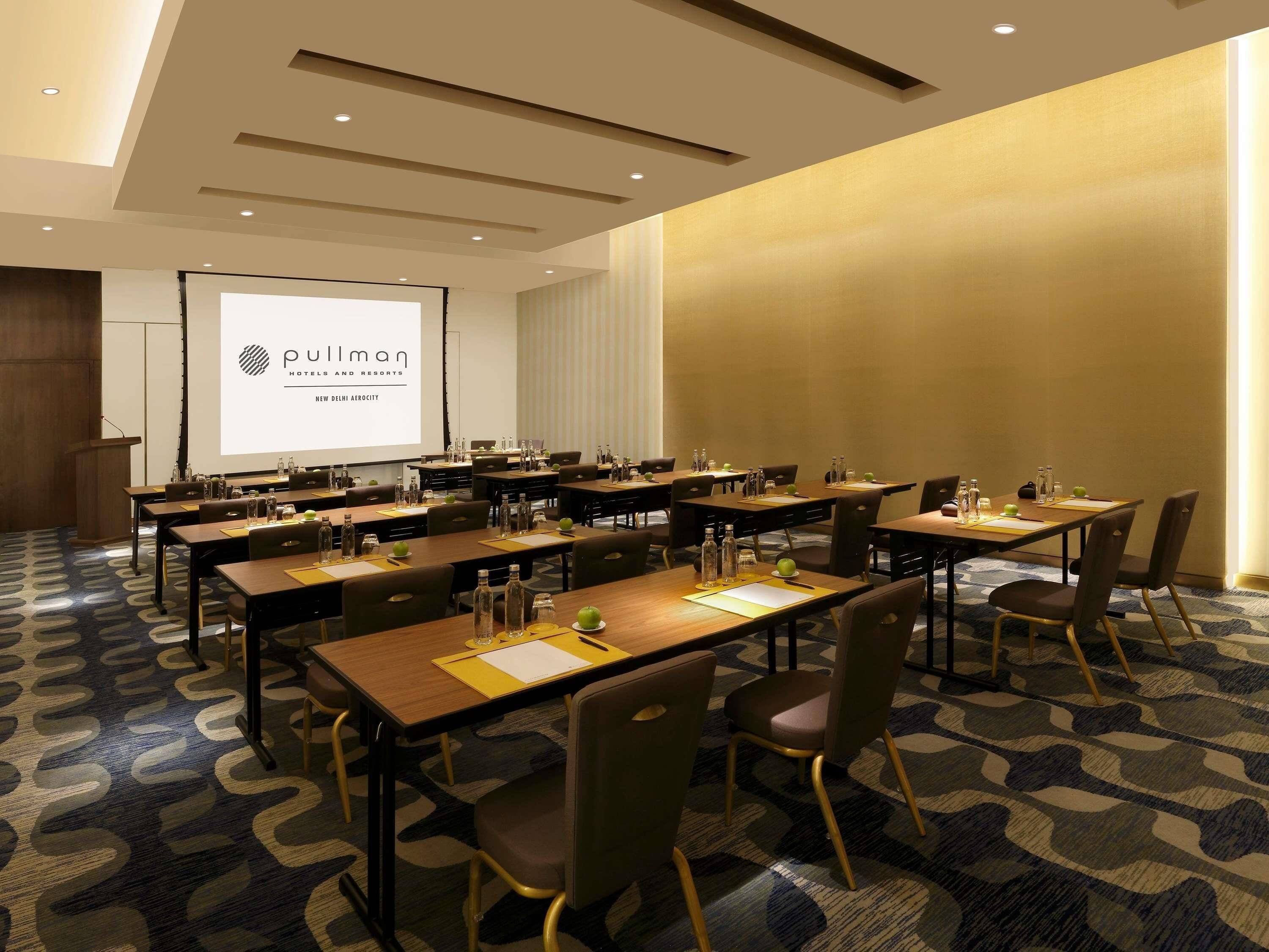 A conference room with multiple tables, chairs, and a presentation screen.
