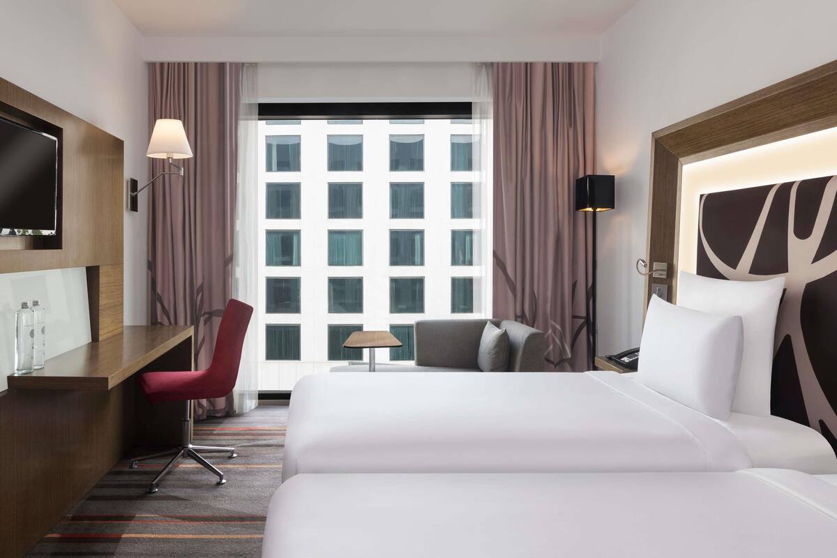 Een hotelkamer met een bed, bureau, stoel, televisie, lamp en uitzicht op een gebouw.