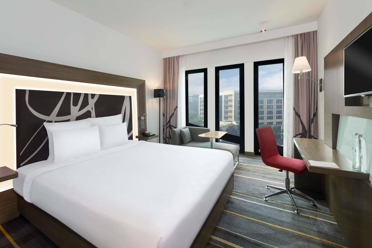 Een hotelkamer met een groot bed, een bureau, een stoel, een klein tafeltje en een televisie.