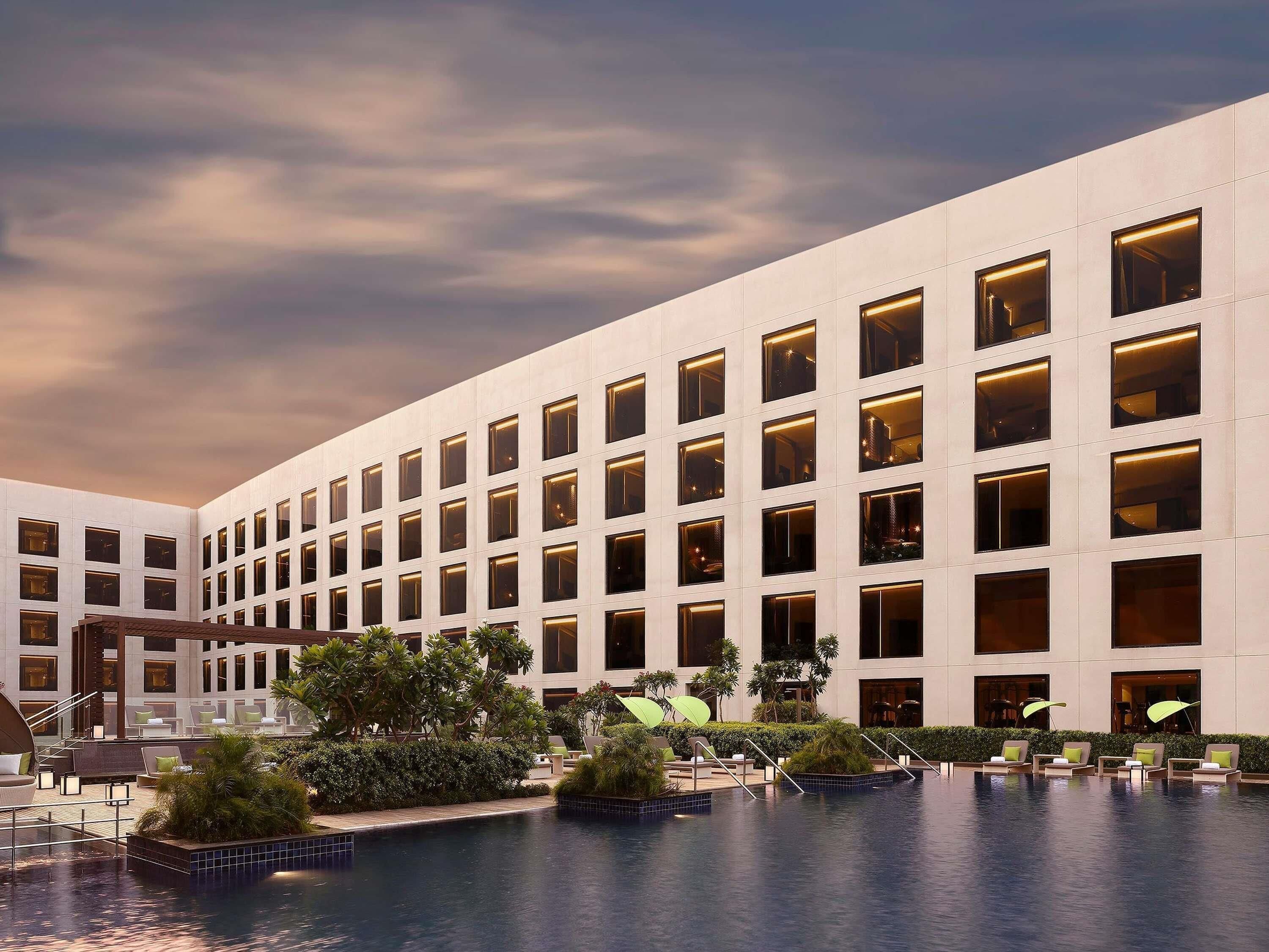 A modern hotel with a pool, multiple floors, and a courtyard with lounge areas.