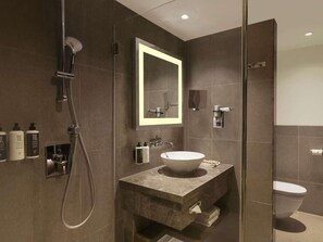 Een moderne badkamer met een douchecabine van glas, een grote spiegel en een wastafel met een waskom.