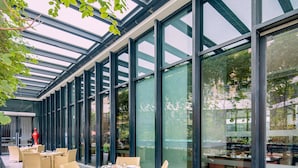 A covered outdoor dining area with wicker furniture and large glass windows.