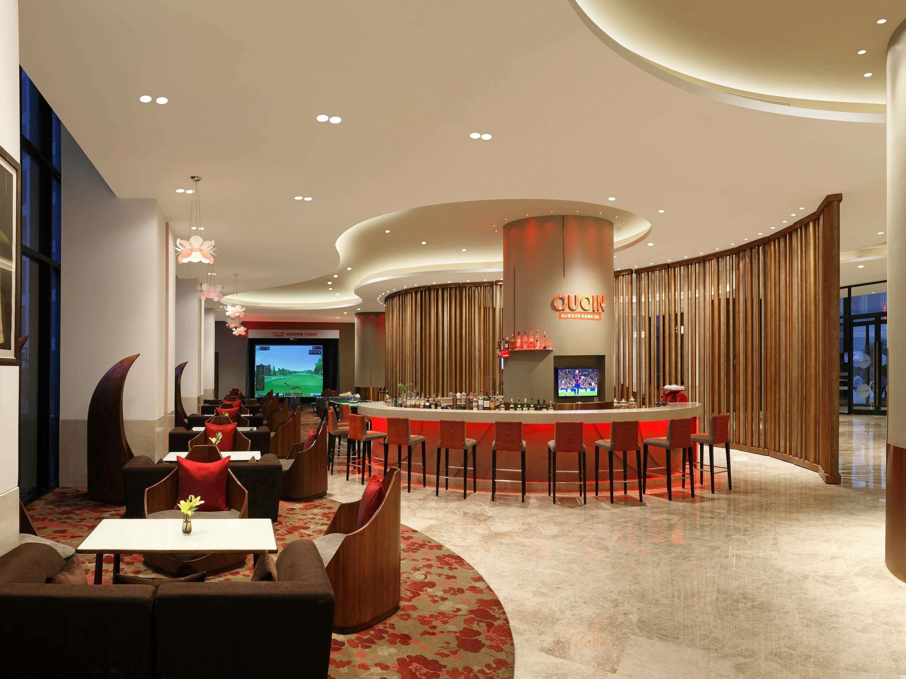 A modern bar area with a curved counter, comfortable seating, and a large screen displaying a golf game.
