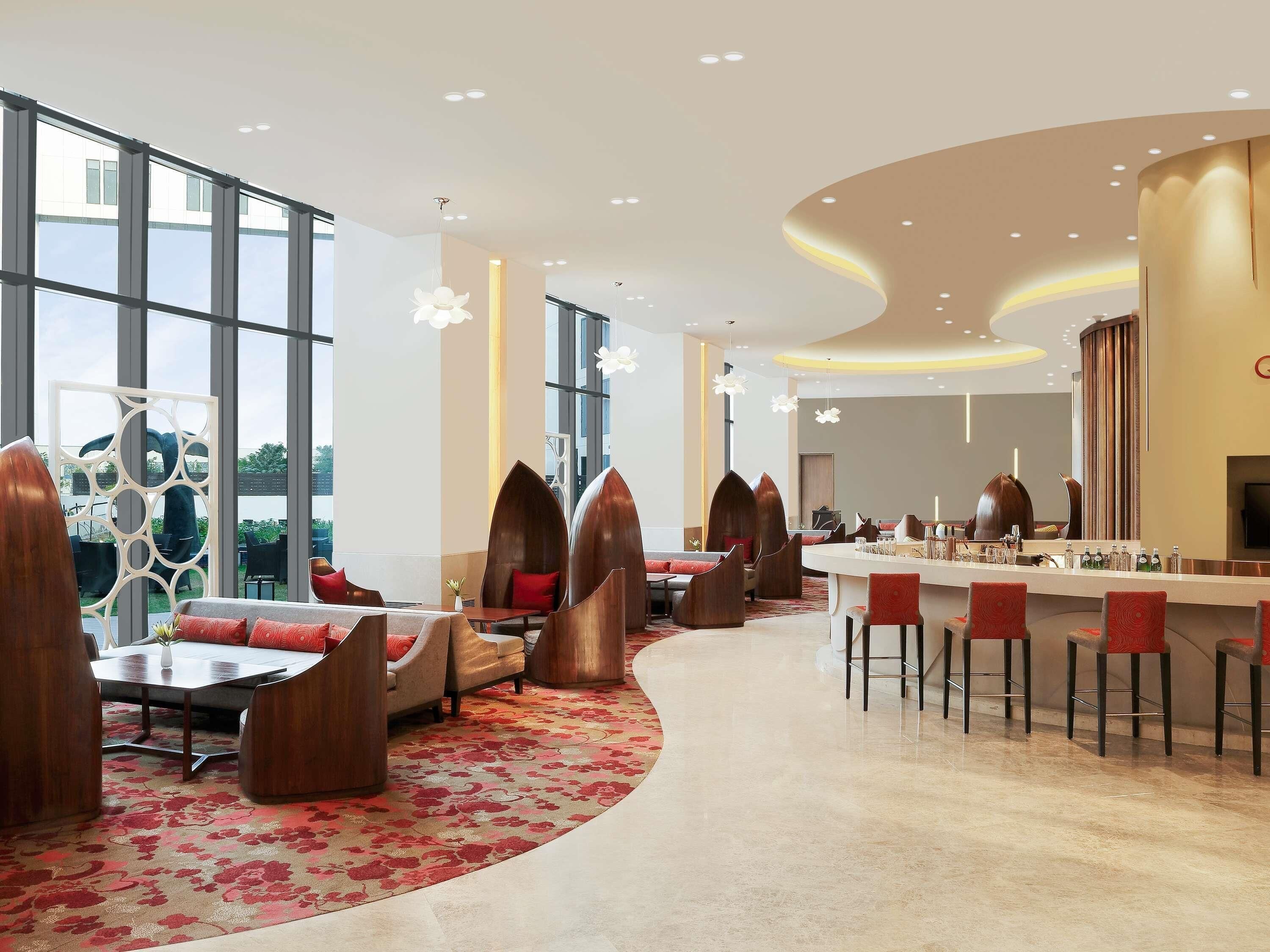 Un hall d’hôtel moderne avec un comptoir d’accueil incurvé, des espaces salon dotés de fauteuils originaux, de grandes fenêtres et un mur décoratif.
