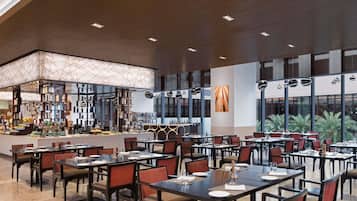 Un restaurante amplio con numerosas mesas y sillas, una zona de bar y grandes ventanales que ofrecen vistas.