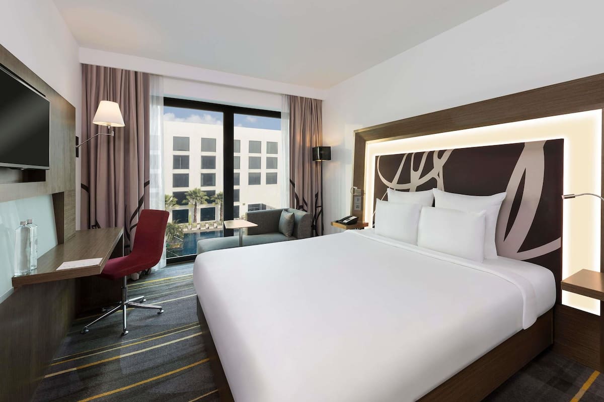Hotelkamer met een groot bed, een bureau met stoel, een televisie en uitzicht op een gebouw en een zwembad.