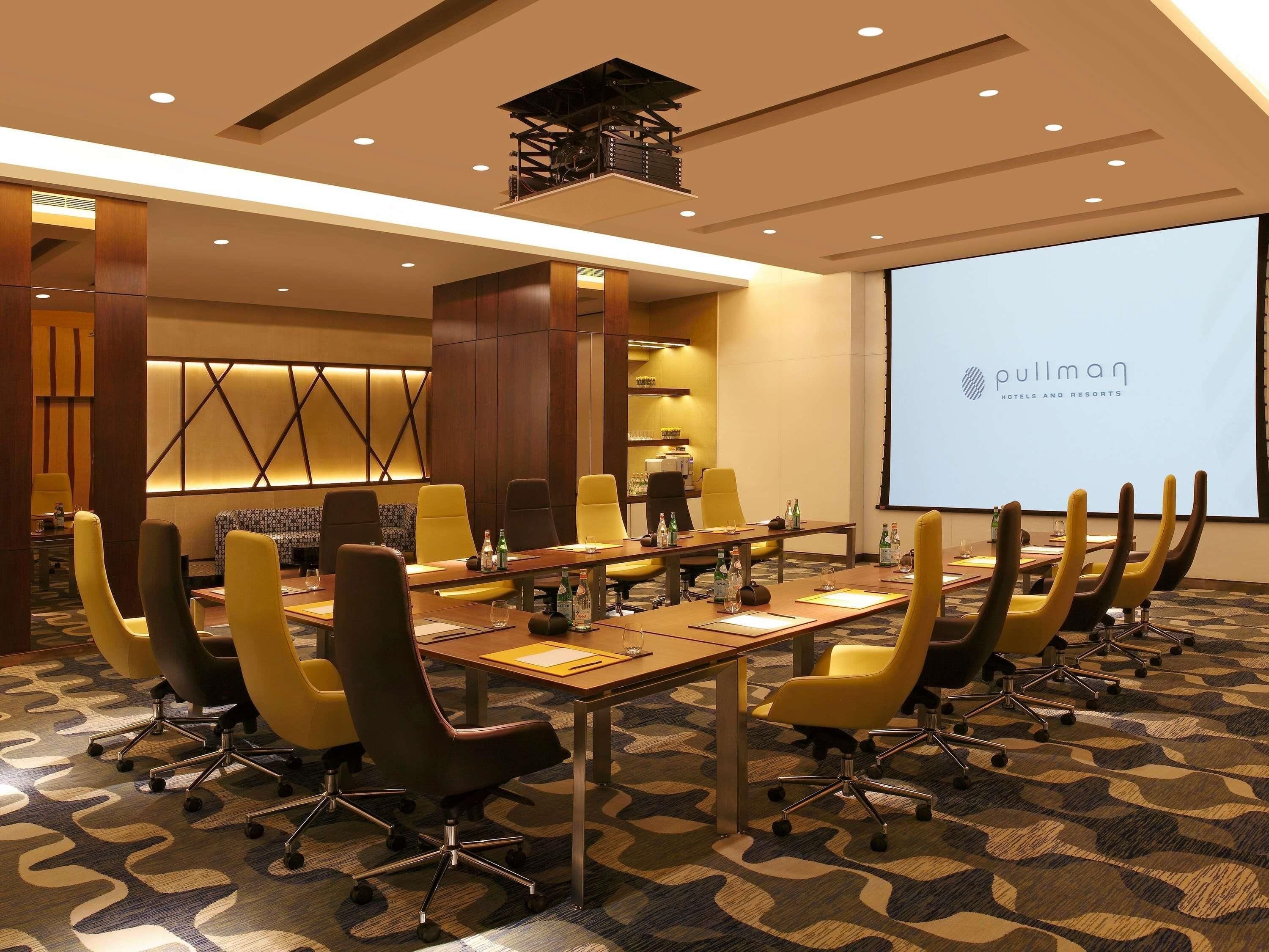 A conference room with a long table, yellow chairs, and a projector screen displaying 'Pullman Hotels and Resorts'.