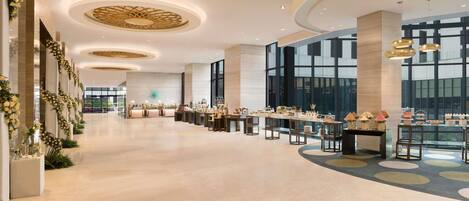 A spacious hotel lobby with a long reception desk, large windows, and a modern ceiling design.