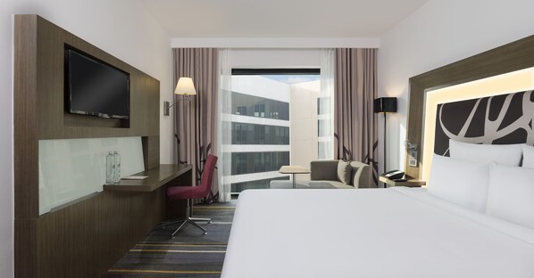 Habitación de hotel con cama, escritorio, televisión, silla, lámpara y vista al exterior.