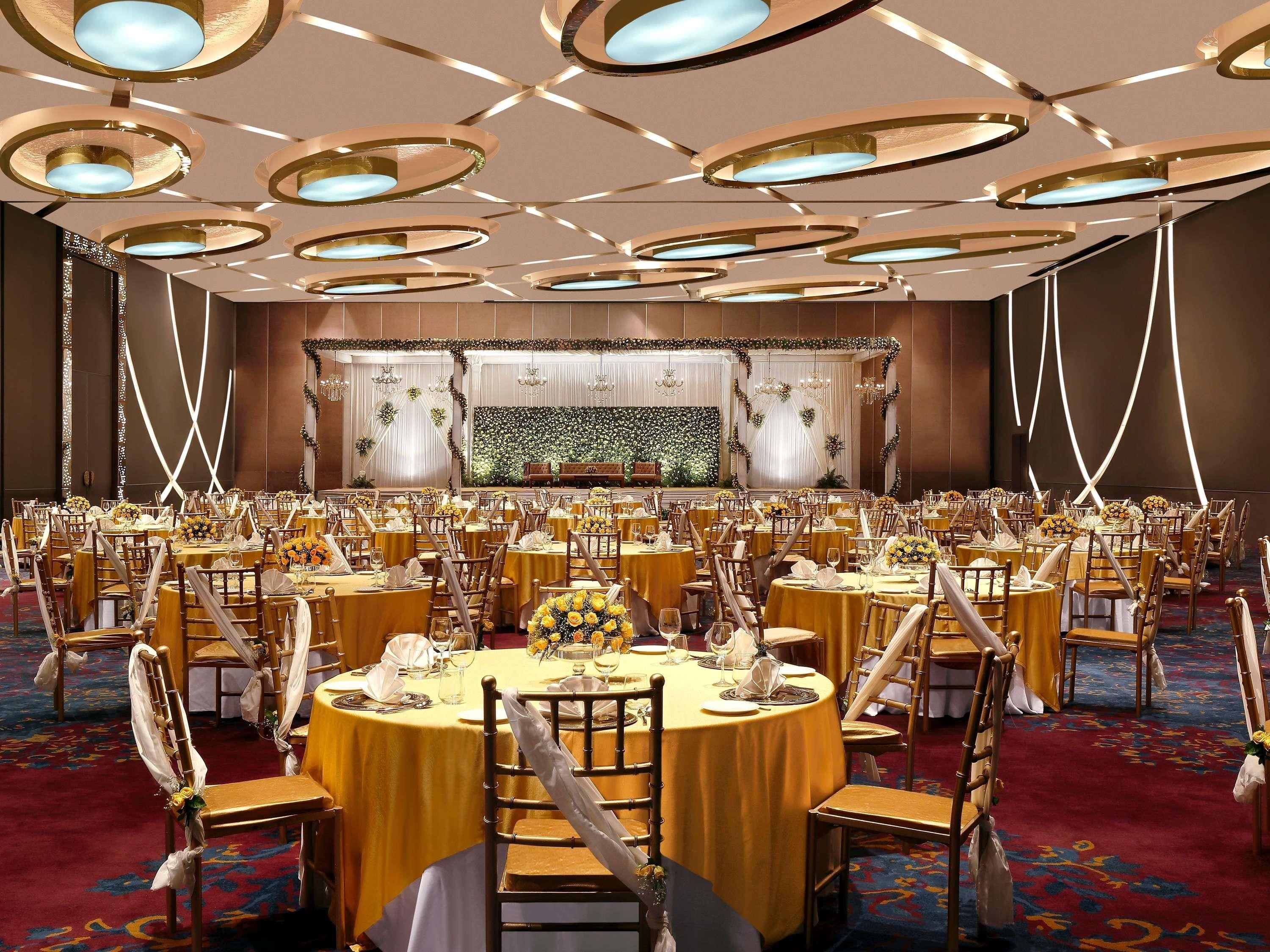 A banquet hall with round tables, chairs, and a stage with floral decorations.