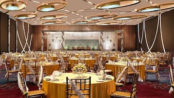 A banquet hall with round tables, chairs, and a stage with floral decorations.
