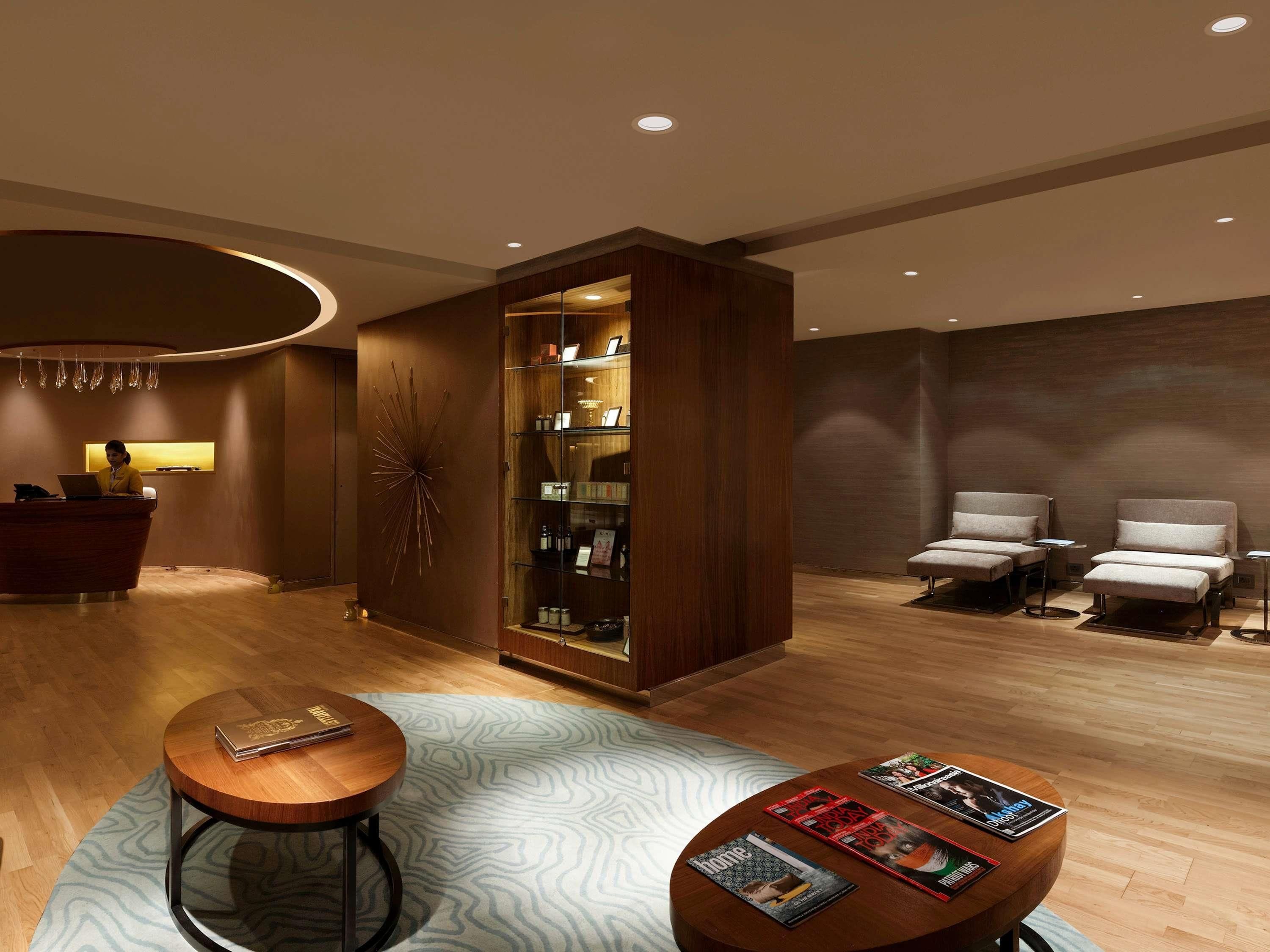 Un vestíbulo de hotel con una recepción, una zona de estar con sillones, una mesa de centro con revistas y una pieza decorativa en la pared.