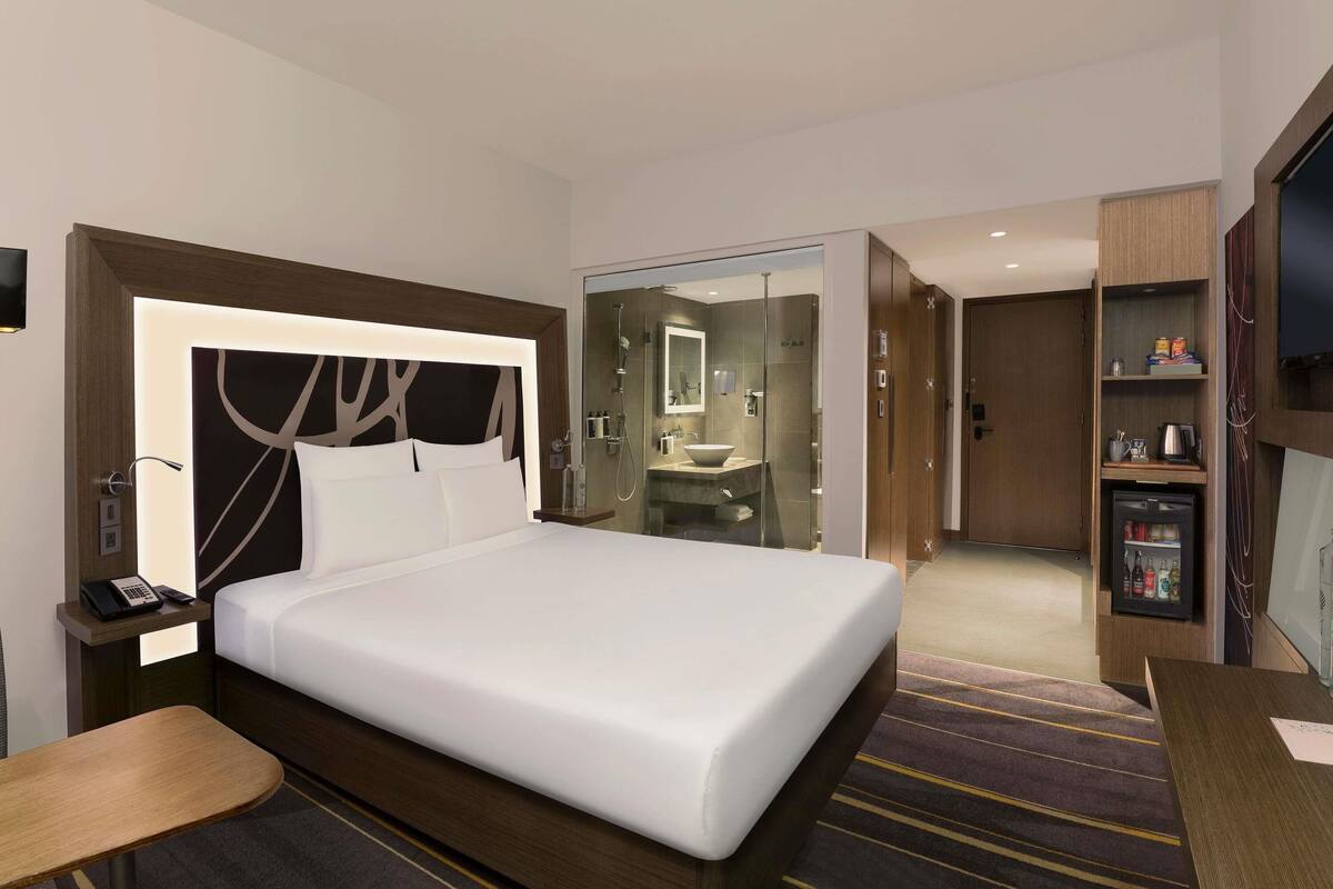 Een moderne hotelkamer met een groot bed, een bureau, een televisie, een minibar en een douchehoek.