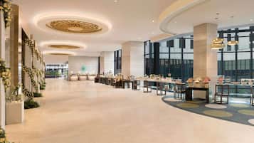A spacious hotel lobby with a long reception desk, large windows, and a modern ceiling design.