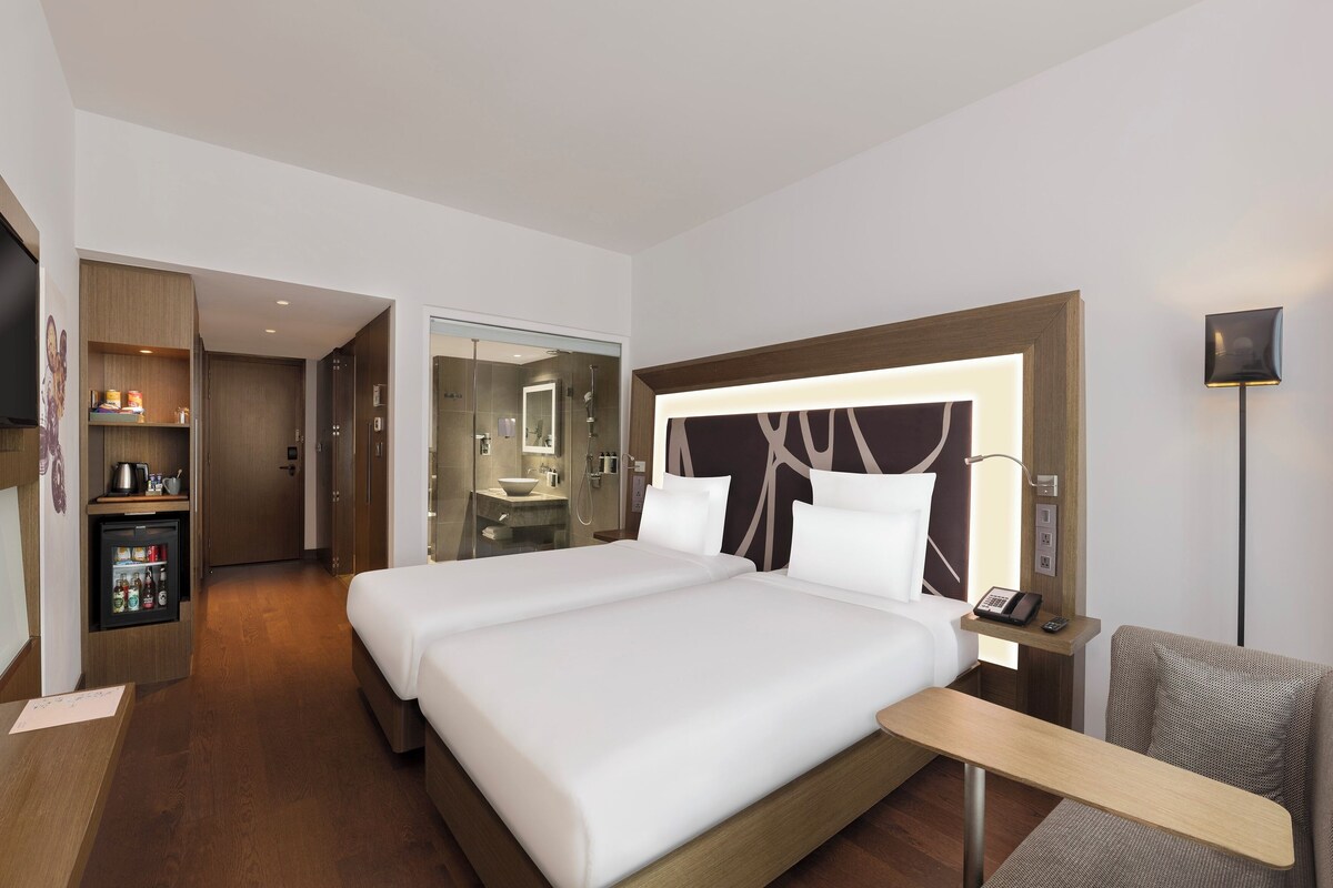 Une chambre d’hôtel avec un grand lit, une table de chevet, une télévision, un bureau et une salle de bain visible à travers une porte ouverte.