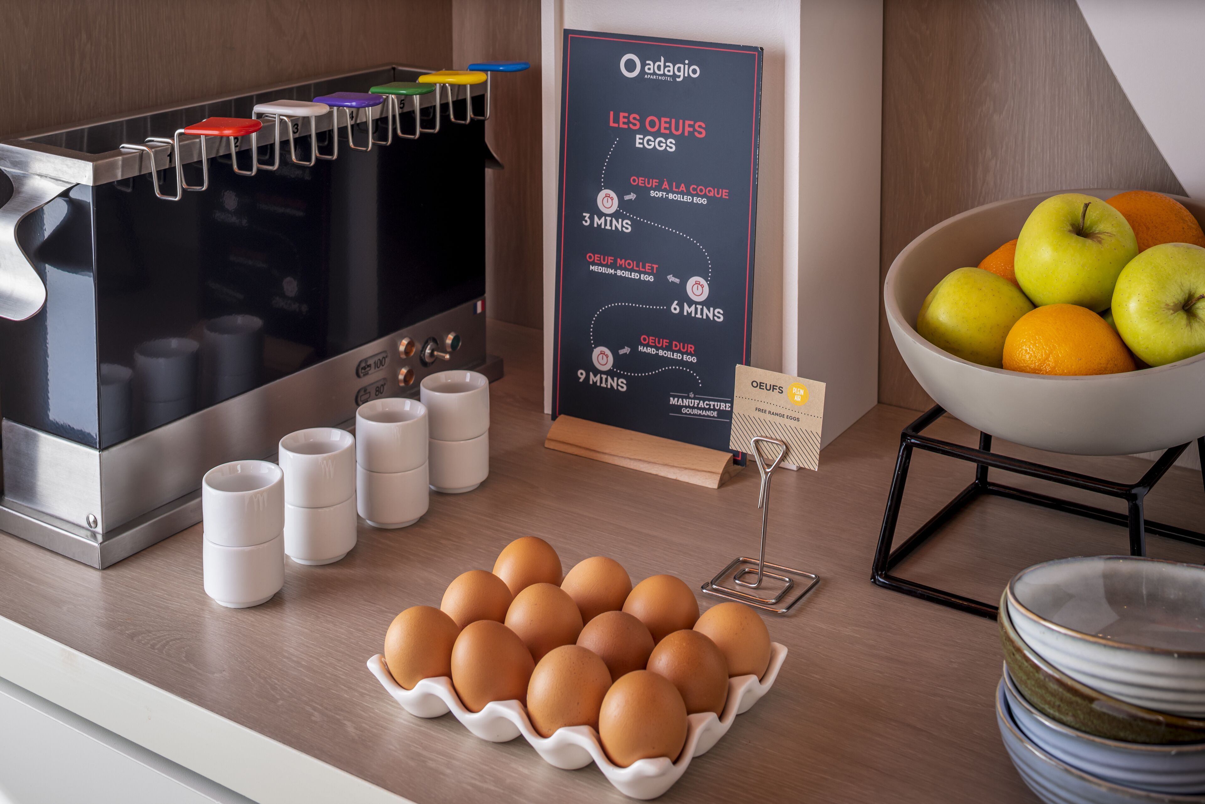 A kitchen counter with a carton of eggs, a coffee machine, and a sign with cooking times.