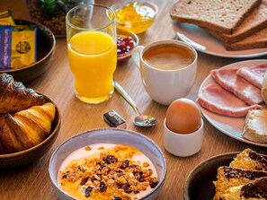 A breakfast table with croissants, orange juice, coffee, eggs, ham, and toast.