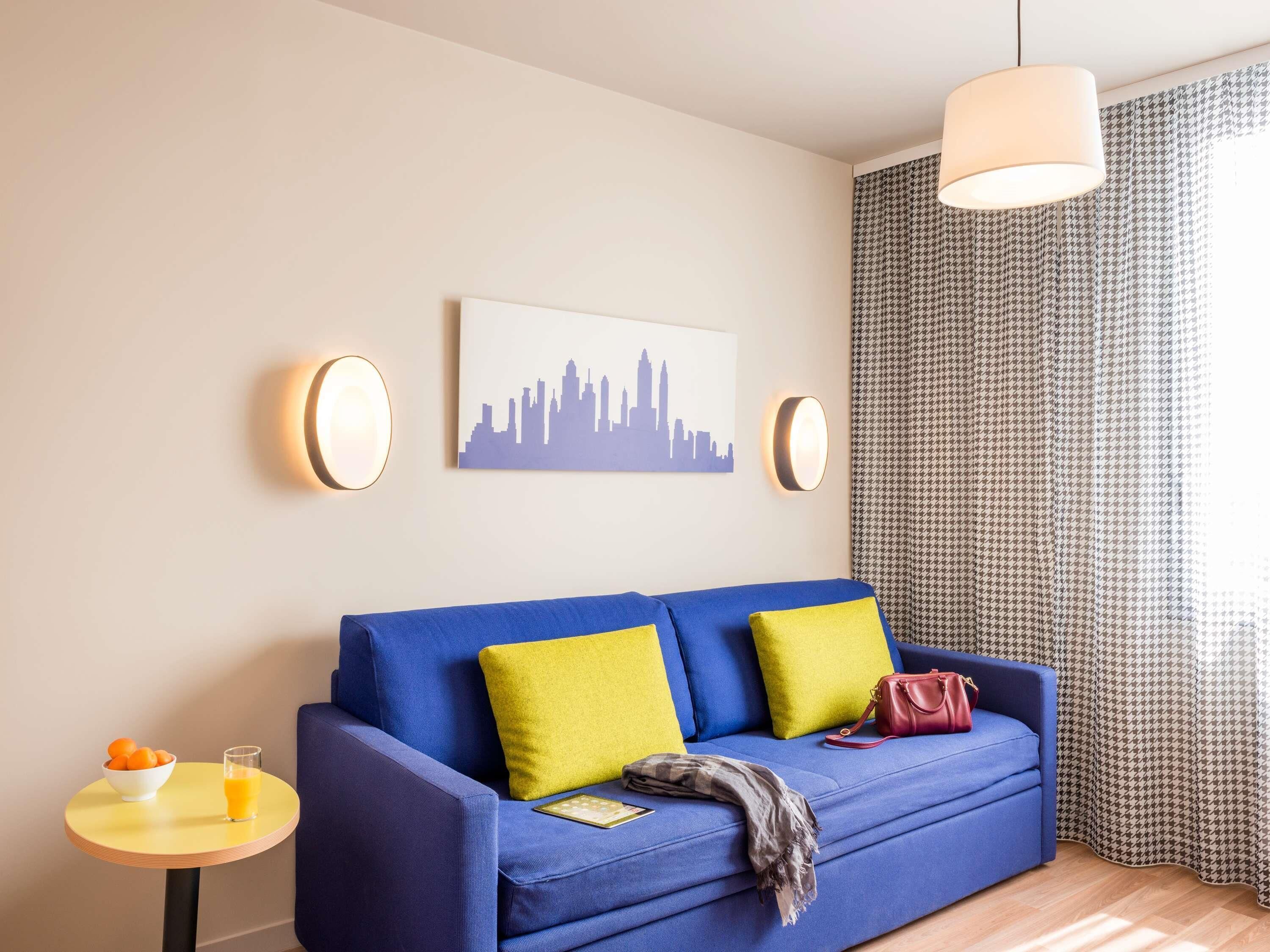 A room with a blue sofa, yellow pillows, a cityscape painting, and a patterned curtain.