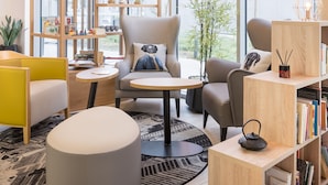 Een modern interieur met een grote boekenkast, comfortabele zitplaatsen en een groot raam met uitzicht op gebouwen.